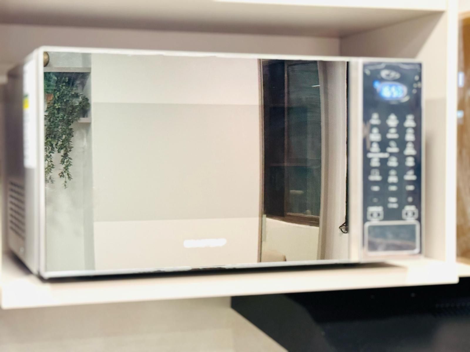 Een magnetron met een digitaal scherm en bedieningspaneel, geplaatst op een witte plank.