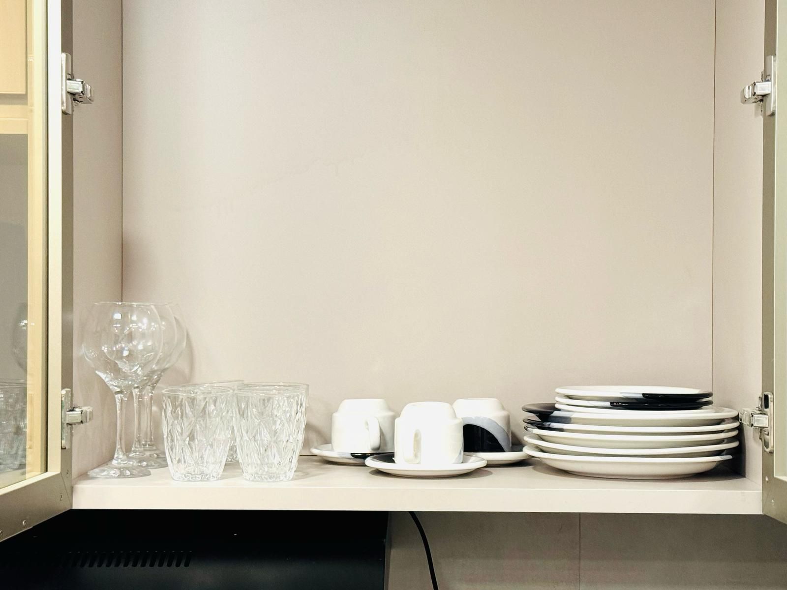 A neatly organized cabinet with clear glassware, white cups, and stacked plates.