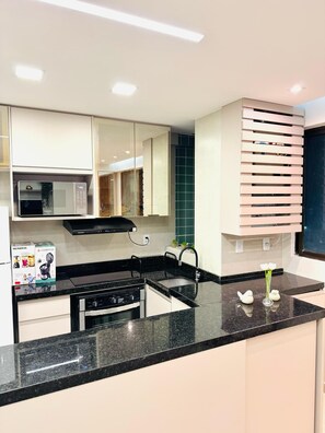A modern kitchen with white cabinets, a black countertop, a microwave, a stove, and a sink.