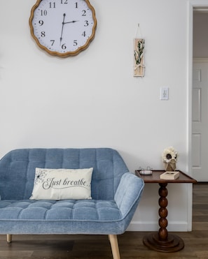 A room with a blue sofa, a wall clock, a small table with a vase, and a door. - CASA AERIE- Amazing Pool View 3rd floor (Phoenix)
