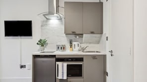 A compact kitchen with a built-in oven, a dishwasher, and a flat-screen TV mounted on the wall. - Sutherland Apartments - Apt 29 (London)