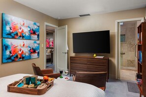 A hotel room with a bed, a TV, artwork on the wall, a wooden dresser, and a bookshelf. - Paradise in the desert (Cathedral City)