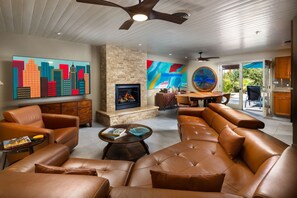 A modern living room with leather sofas, a fireplace, a dining area, and a view through glass doors. - Paradise in the desert (Cathedral City)