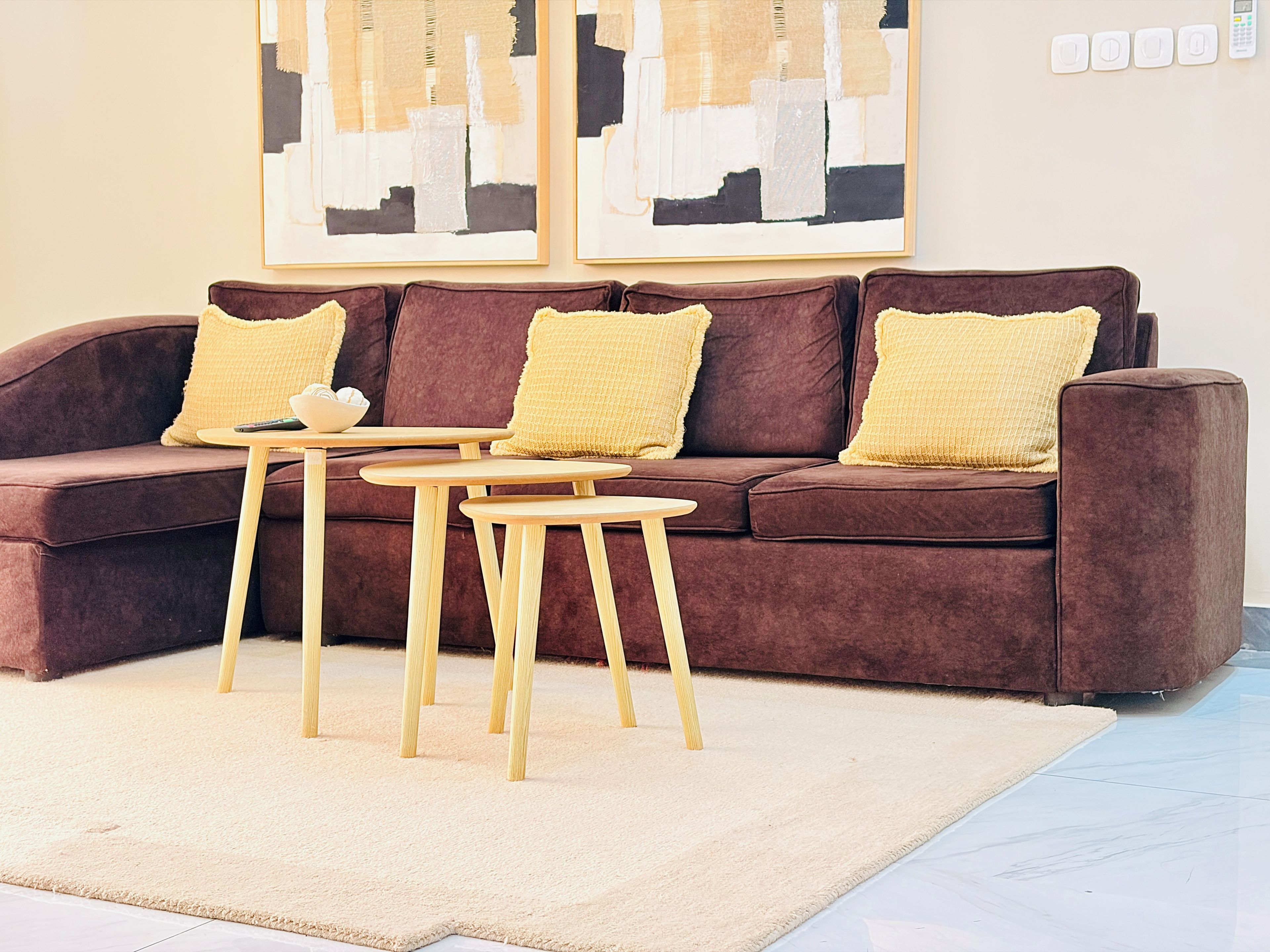 A brown sofa with yellow cushions, two wooden tables, and a beige rug.