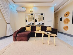 A modern living room with a sectional sofa, two side tables, and abstract wall art. - "Comfort & Elegance" 2-Bedroom Apartment in Bonapriso (Douala)