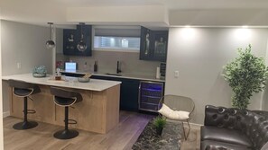 A modern kitchen with a central island, bar stools, dark cabinets, and a seating area with a leather sofa and a chair. - Private 1 bed room with free parking on premises (Calgary)