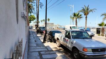 A street with parked vehicles, including a white pickup truck with 'FESACO' on the side, and a white van. There are palm trees and a clear sky.