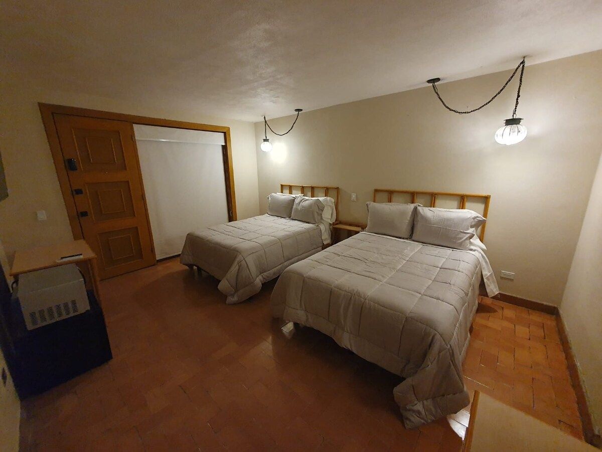 Una habitación con dos camas, una puerta de madera y una pequeña mesa con una caja.