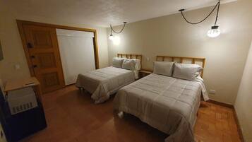A room with two beds, a wooden door, and a small table with a box.