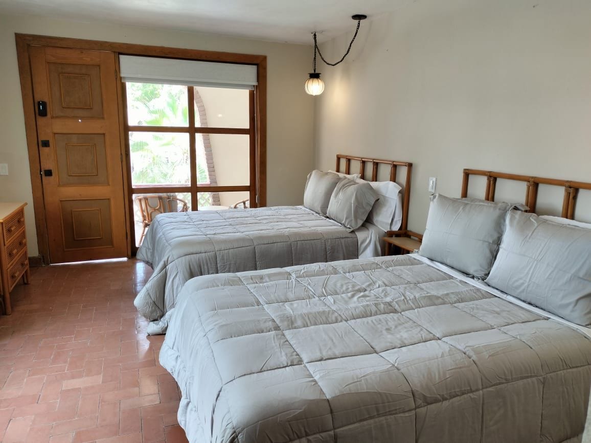 A bedroom with two beds, a wooden door, a window, and a hanging light fixture.