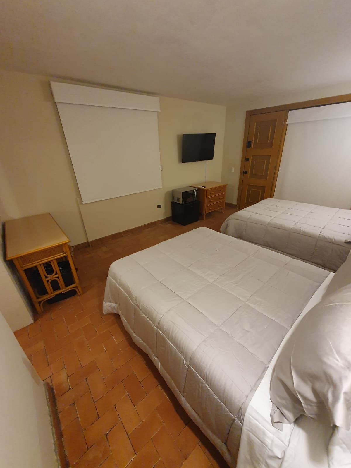 Een kamer met twee bedden, een televisie aan de muur, een houten deur en een klein tafeltje.