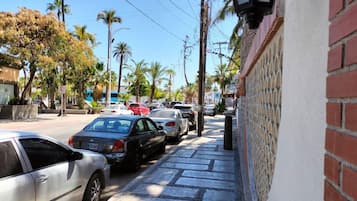 A street with parked cars, a sidewalk, and a building with a brick facade.