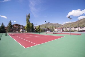 En tennisbane med net, omgivet af bygninger og træer.