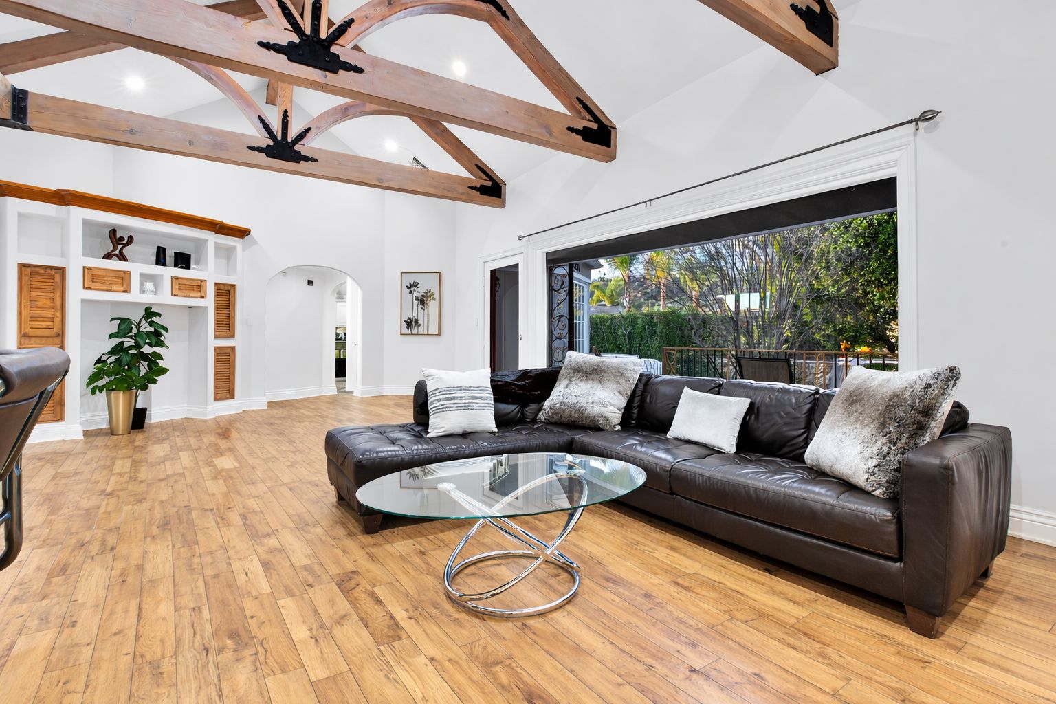 Un salon spacieux avec un canapé en cuir, une table basse en verre, un plancher en bois et une grande fenêtre donnant sur un paysage verdoyant.