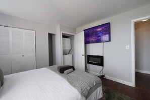 A bedroom with a bed, a television mounted on the wall, a closet, and a door leading to another room. - Cozy 2BR : Forest Park • WashU • Delmar Loop (St. Louis)