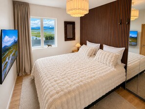 Un dormitorio con una cama grande, una ventana con vistas, un cabecero de madera y un espejo.