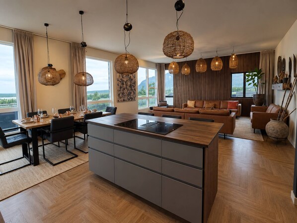 Una cocina moderna con una isla central, comedor con mesa y sillas, y sala de estar con sofá y un amplio ventanal con vistas panorámicas.
