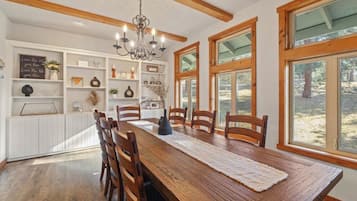 A dining area with a wooden table, chairs, a chandelier, and large windows.