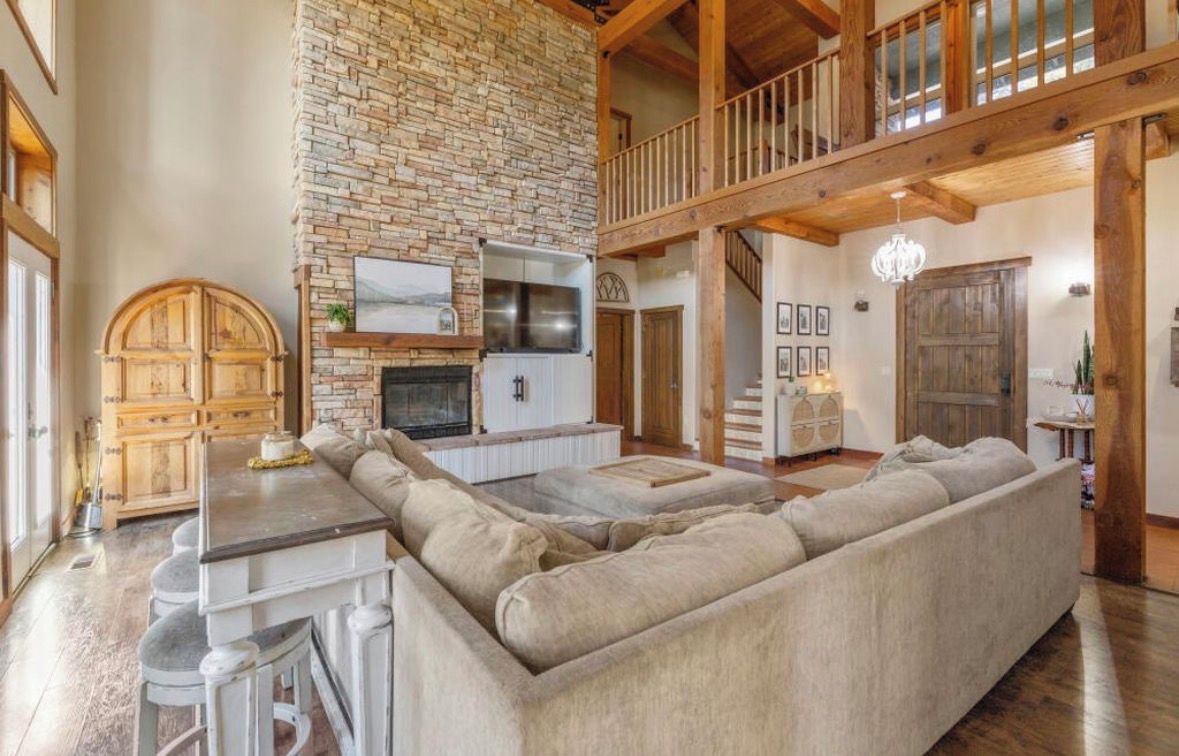 A spacious living area with a stone fireplace, a large sectional sofa, and a wooden ceiling.