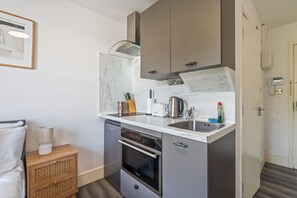 A compact kitchenette with a built-in oven, a sink, and a microwave. - Sutherland Apartments - Apt 31 (London)