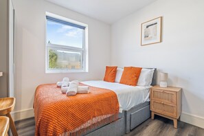 A hotel room with a bed, a nightstand, a framed picture on the wall, and a window with a view of the outside. - Sutherland Apartments - Apt 31 (London)