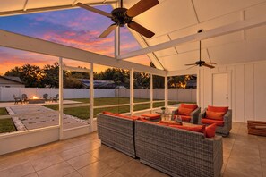 Eine überdachte Terrasse im Freien mit Sitzgelegenheit, Deckenventilator und Blick auf den Garten.
