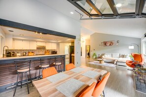 A modern kitchen with a bar area, a dining table with chairs, and a living area with a sofa and a chair. - The Warm Timber Retreat (Vancouver)