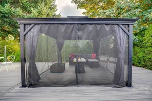 A covered outdoor seating area with a fire feature, surrounded by greenery. - The Warm Timber Retreat (Vancouver)
