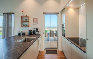 A modern kitchen with a view to the outdoors, a coffee machine, and a dining area with a table and chairs. - Lovely home in Lemvig with sauna (Lemvig)