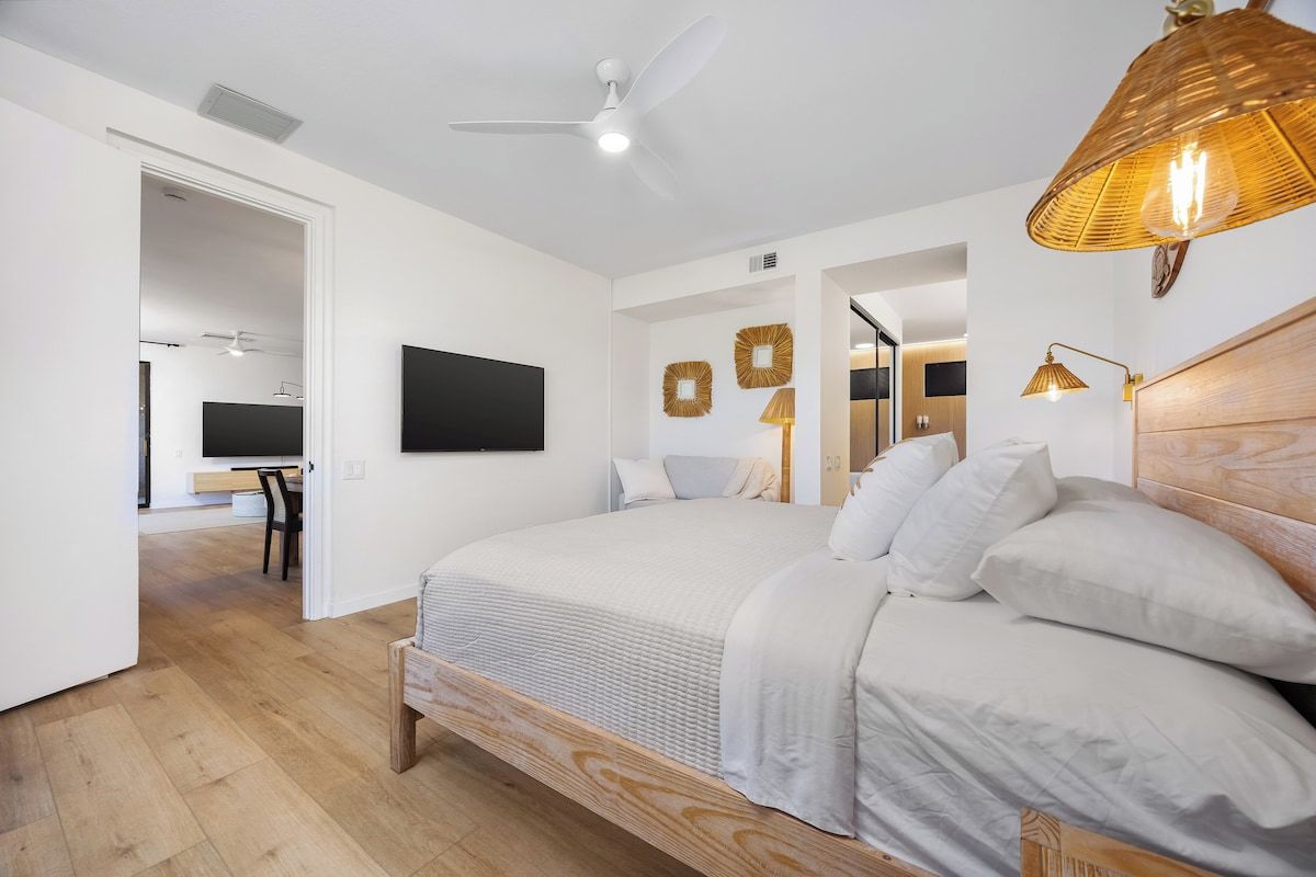 Une chambre moderne avec un grand lit, un ventilateur de plafond et un téléviseur en arrière-plan.