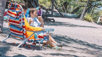 A beach scene with a striped beach chair and a person sitting in it.