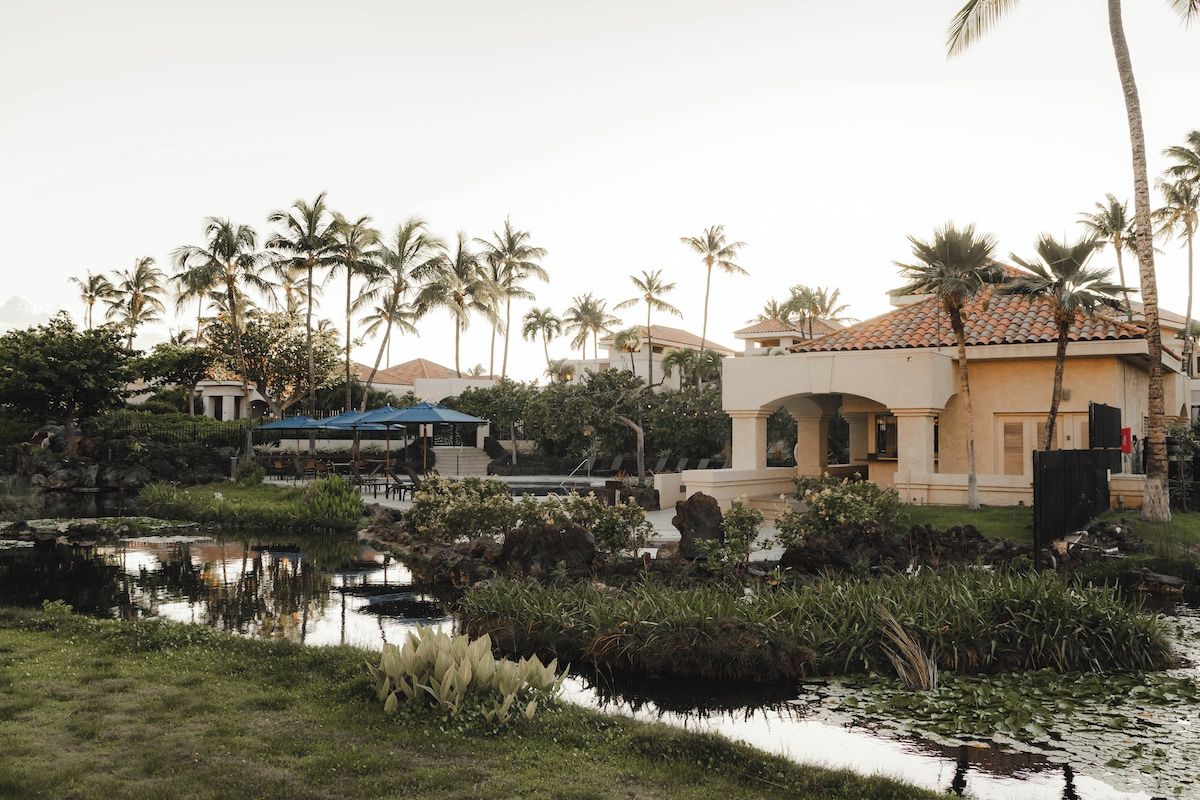A resort with a pool, palm trees, and a building with a tiled roof.