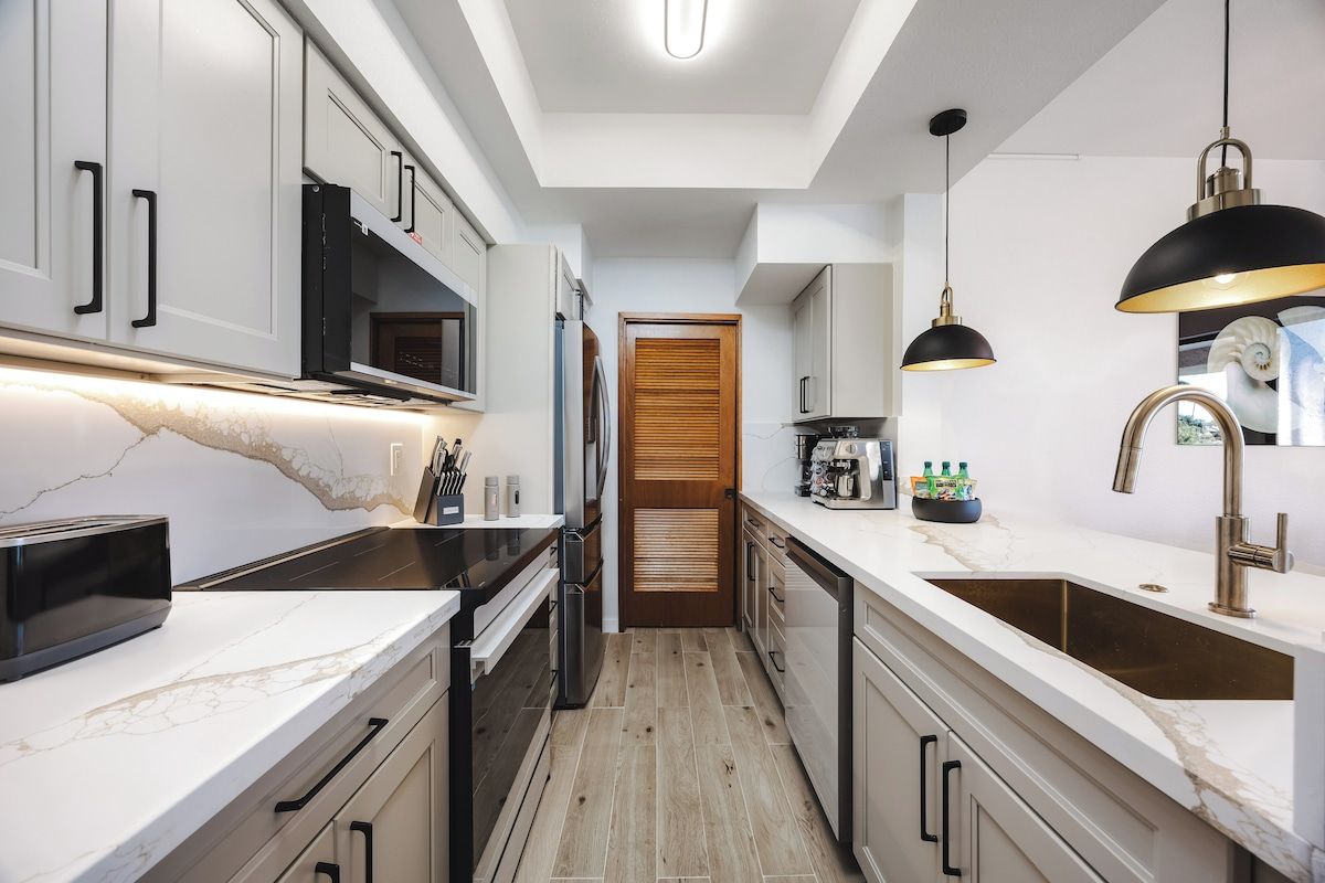 A modern kitchen with white cabinetry, a marble countertop, and a black pendant light.