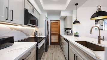 A modern kitchen with white cabinetry, a marble countertop, and a black pendant light.