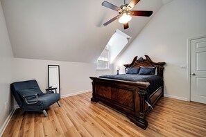Ein Schlafzimmer mit geneigter Decke, einem Bett mit Holz-Kopfteil, einem Stuhl und einem Nachttisch mit Lampe.