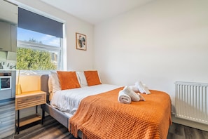 A bedroom with a bed, a nightstand, a window, and a radiator. - Sutherland Apartments - Apt 32 (London)