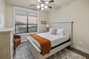 Une chambre à coucher comprenant un lit, une table de chevet, une commode, une fenêtre avec vue et un ventilateur de plafond.