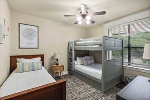 A room with a bunk bed, a single bed, a ceiling fan, a window with blinds, and a framed map on the wall. - Hilltop Lake Views | Hollows Resort Amenities (Jonestown)