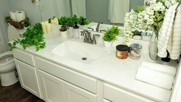 Un bagno con lavandino bianco, due rubinetti, uno specchio e diversi articoli da toilette.