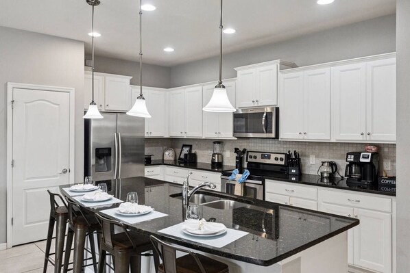 A modern kitchen with white cabinetry, stainless steel appliances, and a central island with bar stools. - Private Pool + Star Wars Game Room + Arcade Loft | Near Disney (Kissimmee)