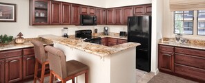 Una cocina con gabinetes de madera oscura, un refrigerador negro, encimeras de granito y una isla integrada con taburetes de bar.