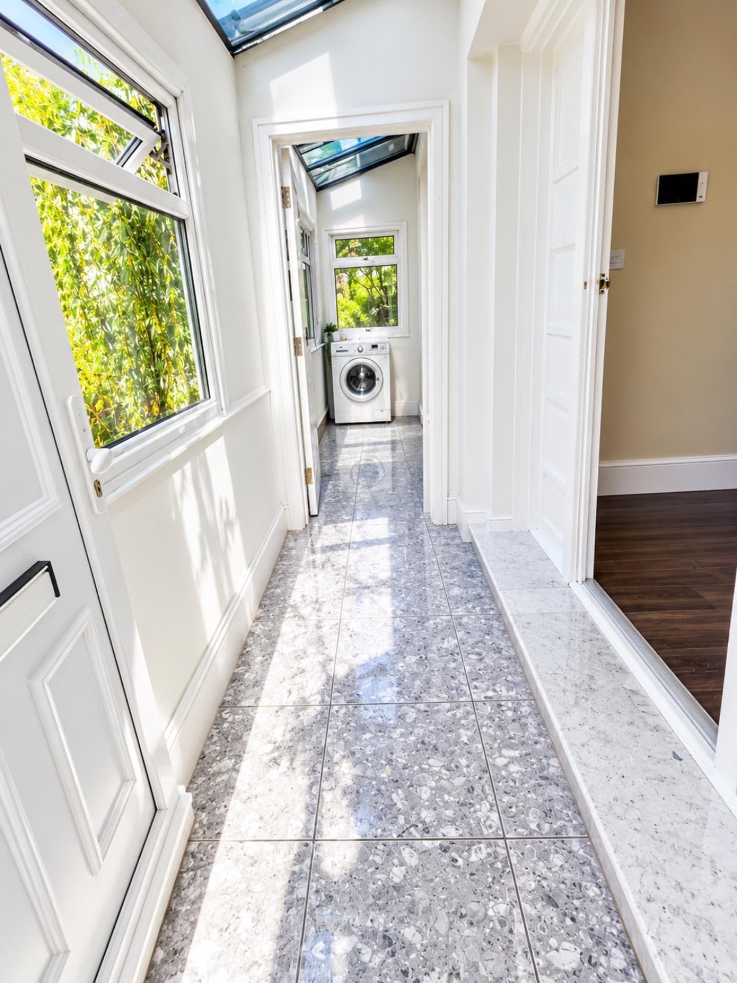 A hallway with a washing machine, a door, and a window with a view of greenery.
