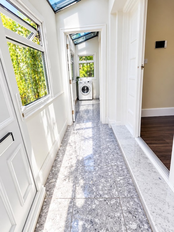 A hallway with a washing machine, a door, and a window with a view of greenery. - Apartment Sleeps 6 With Wifi (Wembley)