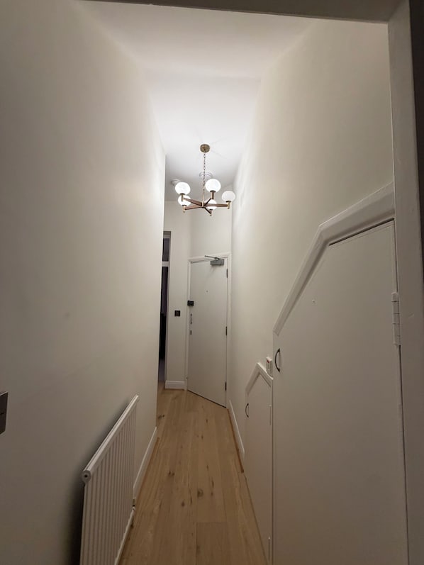 A narrow hallway with a wooden floor, white walls, and a ceiling light fixture.