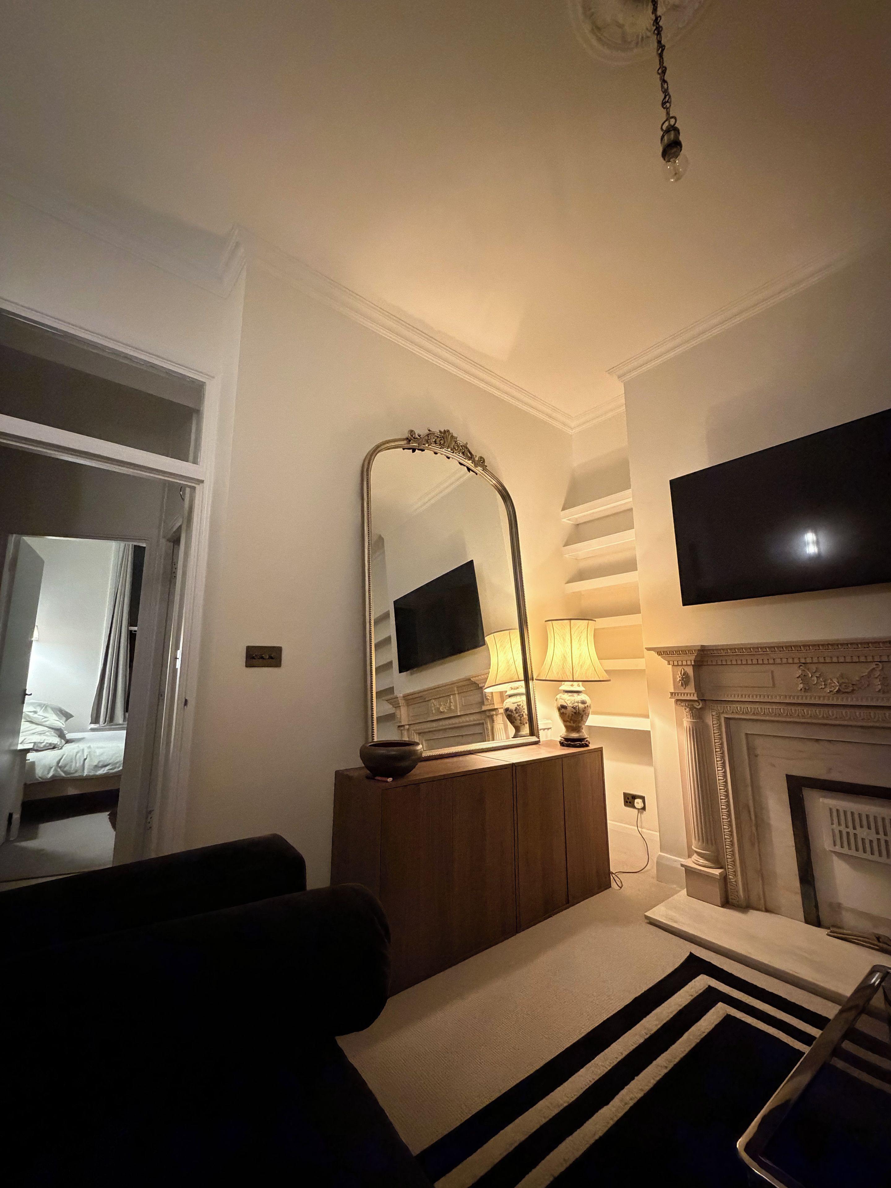 A hotel room with a bed, a television mounted on the wall, a fireplace, and a mirror with a decorative frame.