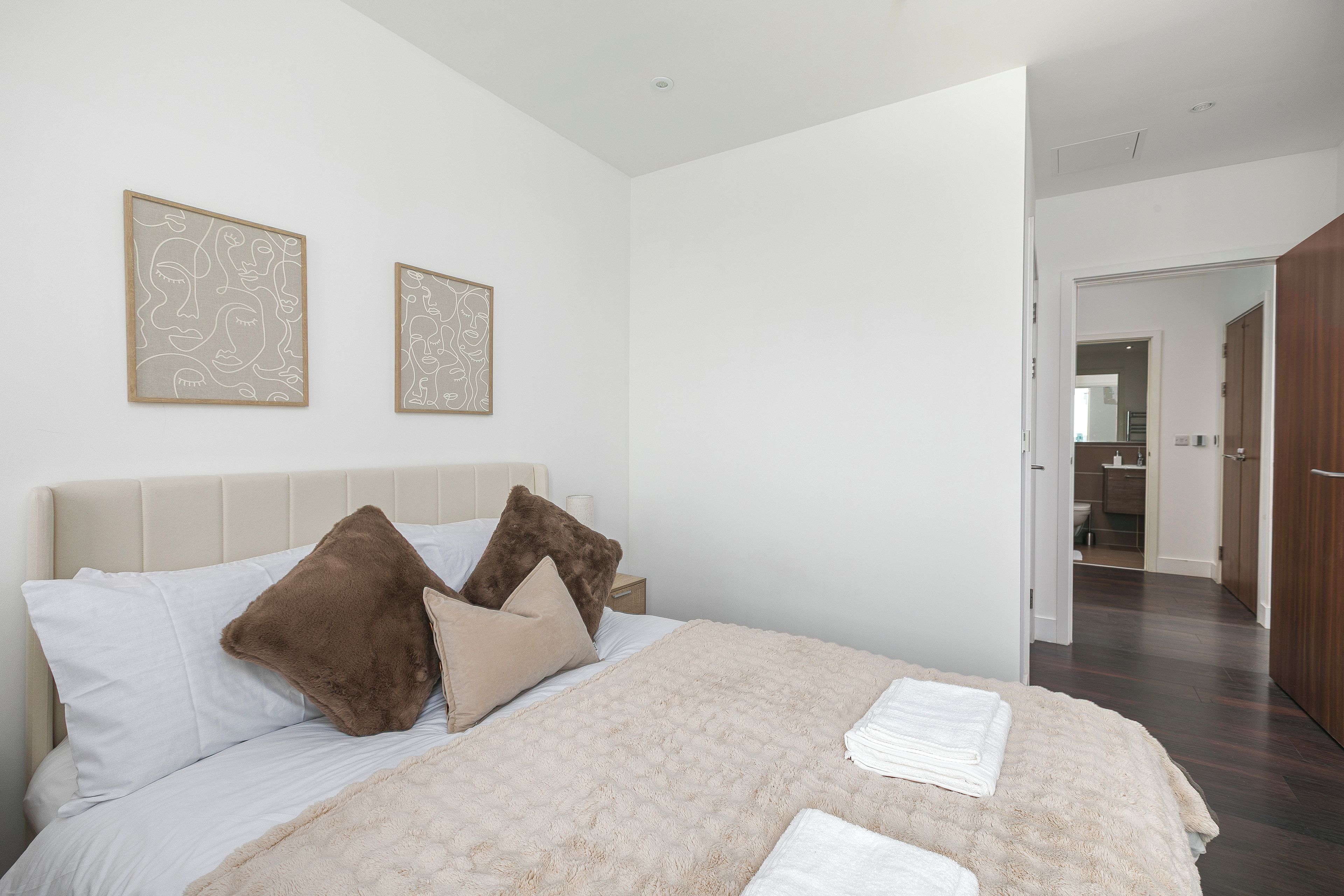 A bedroom with a bed, pillows, a bedside table, and two framed artworks on the wall.