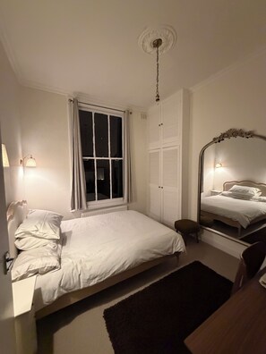A bedroom with a bed, a bedside table, a mirror, a window with curtains, and a ceiling light fixture. - Beautiful flat in Ealing - 4 min walk to station (London)