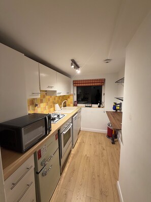 A compact kitchen with white cabinets, a microwave, an oven, and a sink. - Beautiful flat in Ealing - 4 min walk to station (London)