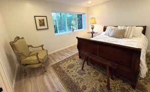 A bedroom with a large bed, a chair, a window, and a lamp. - 5 minutes to the beach! The Hideaway on Lillie Ave. (Summerland)