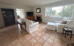 A living room with a fireplace, a television, and a window with a view of greenery. - 5 minutes to the beach! The Hideaway on Lillie Ave. (Summerland)